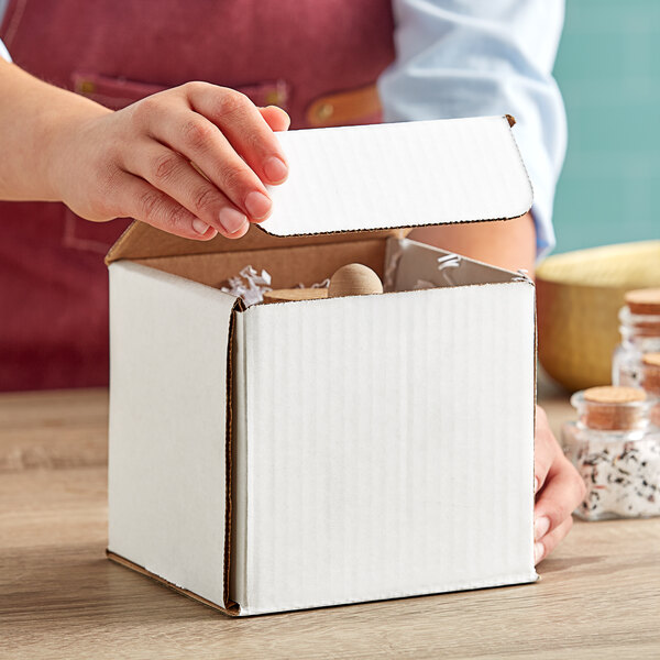 A person opening a Lavex white corrugated mailer box with a small object inside.