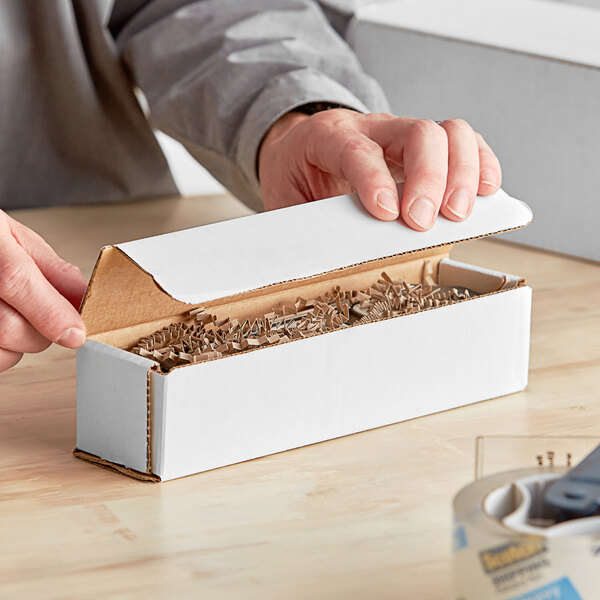 A person using a hand to open a white Lavex corrugated mailer.