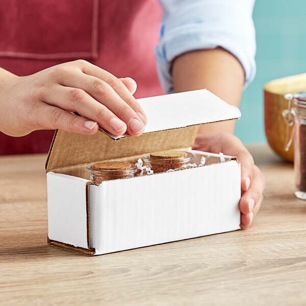 A person opening a white Lavex corrugated mailer box with small glass jars inside.