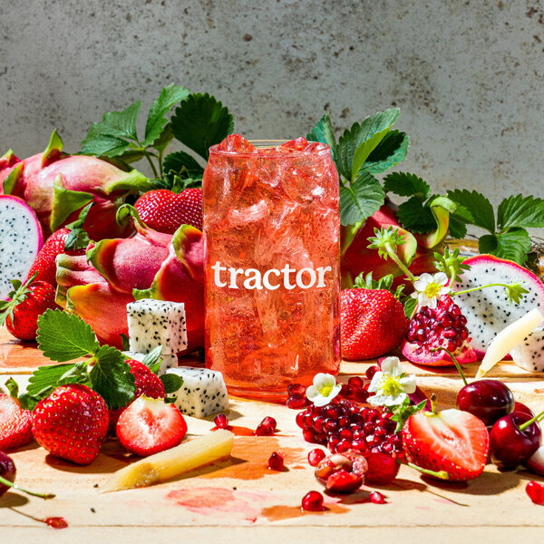 A glass of Tractor Beverage Co. strawberry dragon fruit juice concentrate surrounded by strawberries and dragon fruit.