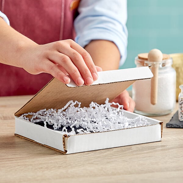 A person's hand opening a Lavex white cardboard mailer box with shredded paper inside.