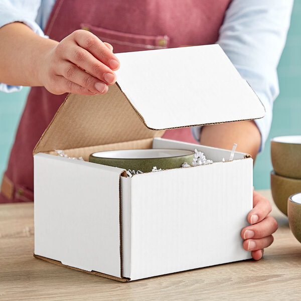 A person opening a Lavex white corrugated mailer box to reveal a bowl inside.