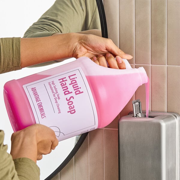 A gallon container of Advantage Chemicals ready-to-use pink liquid hand soap being poured into a wall-mounted soap dispenser.