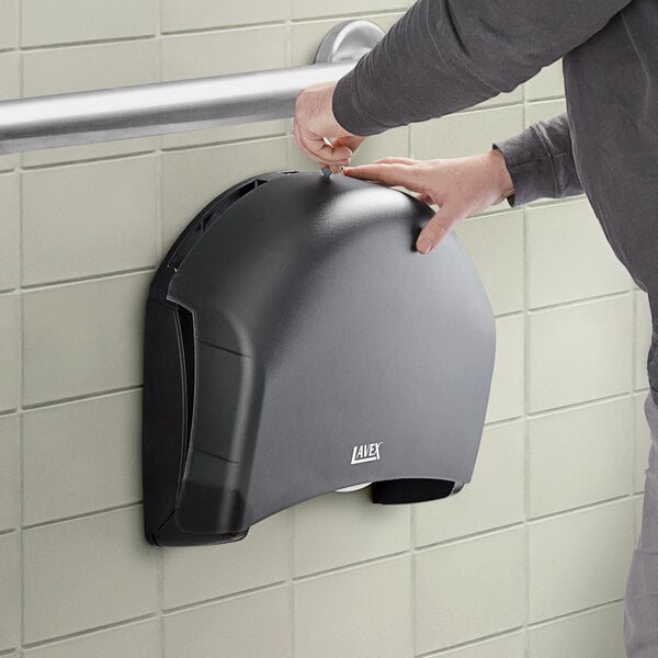 A person using a Lavex black single roll jumbo toilet tissue dispenser.