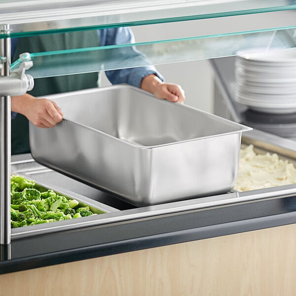 A person holding a Vigor aluminum steam table spillage pan with food in it.