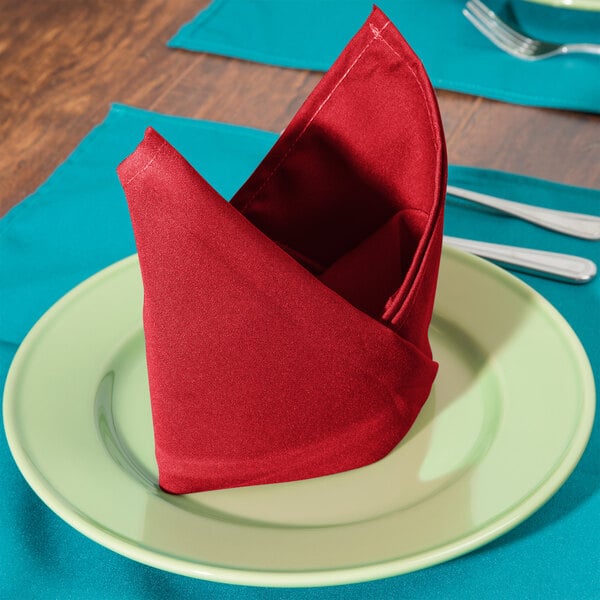 A folded red Intedge cloth napkin on a plate.