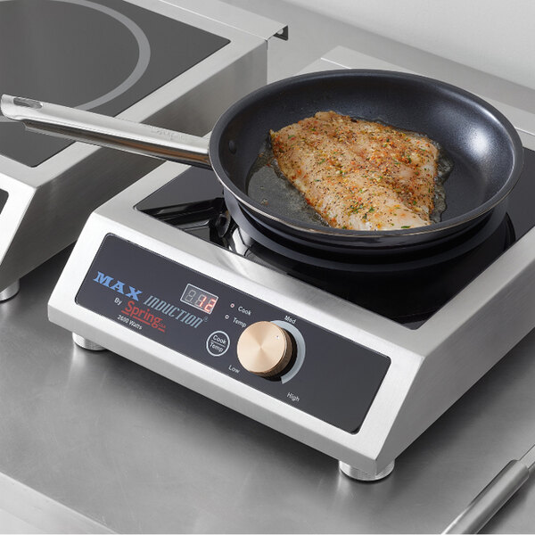 A non-stick fry pan with a stainless steel handle containing a seasoned fish fillet, placed on an induction cooktop.