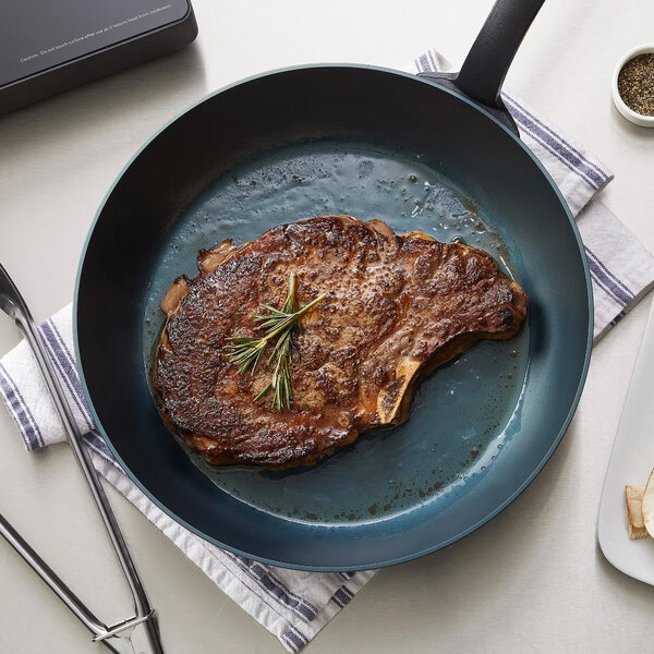A large carbon steel fry pan containing a cooked steak garnished with rosemary.