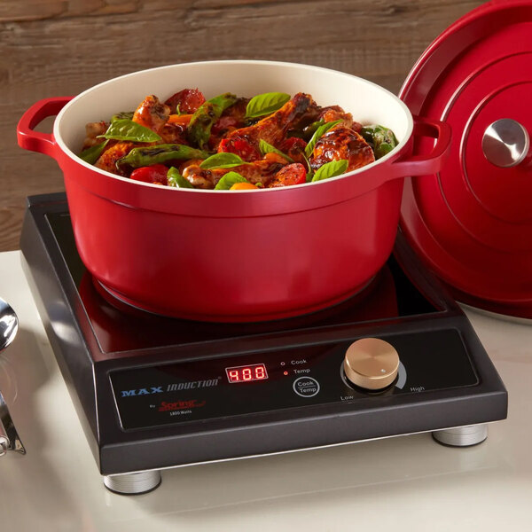 A red non-stick round casserole dish with a cover, filled with food, placed on an induction cooktop.