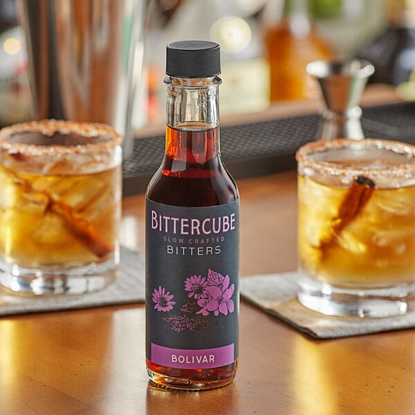 A bottle of Bittercube Bolivar Bitters on a table next to two glasses of liquid.