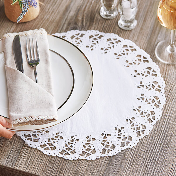 A person holding a plate with a Hoffmaster lace doily, a fork, and a glass of wine.
