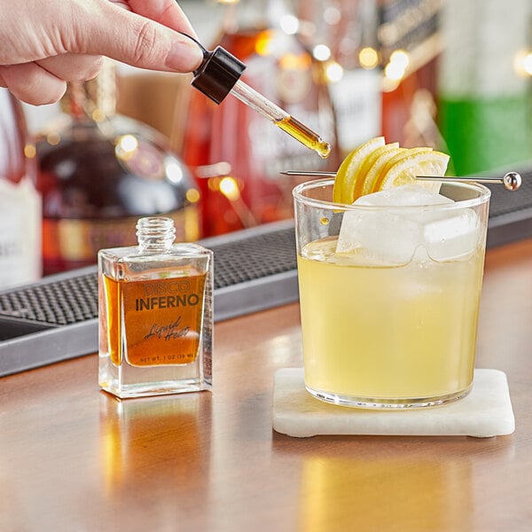 A hand using a dropper to add Bittercube Disco Inferno Liquid Heat Tincture to a cocktail.