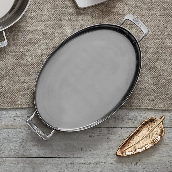 An oval stainless steel saute pan with two handles.