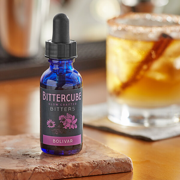 A blue bottle of Bittercube Bolivar Bitters on a marble surface next to a drink.