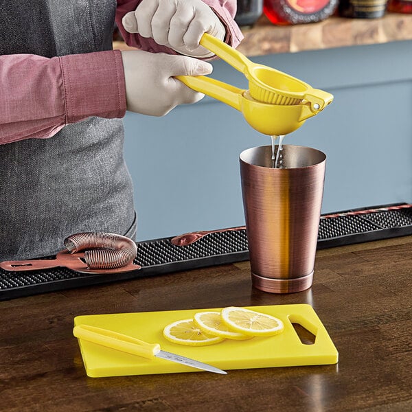 A person using yellow tongs to squeeze a lemon slice over a glass.