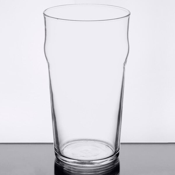 An Arcoroc English pub glass filled with beer on a white surface.