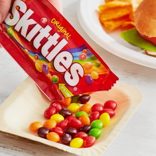 A hand holding a SKITTLES® Original Fruity Candies pouch.