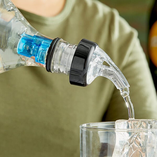 A person using a Choice 3-Ball Measured Liquor Pourer to pour liquid into a glass on a table in a cocktail bar.