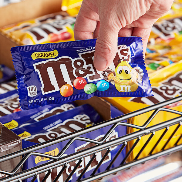 A hand holding a small package of M&M's Caramel Milk Chocolate Candies.