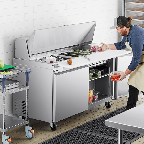 A man in a commercial kitchen using an Avantco stainless steel sandwich prep table.