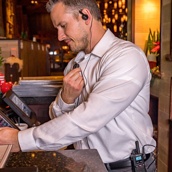 A person using a Midland FRS two-way business radio with an earpiece and microphone in a professional setting.