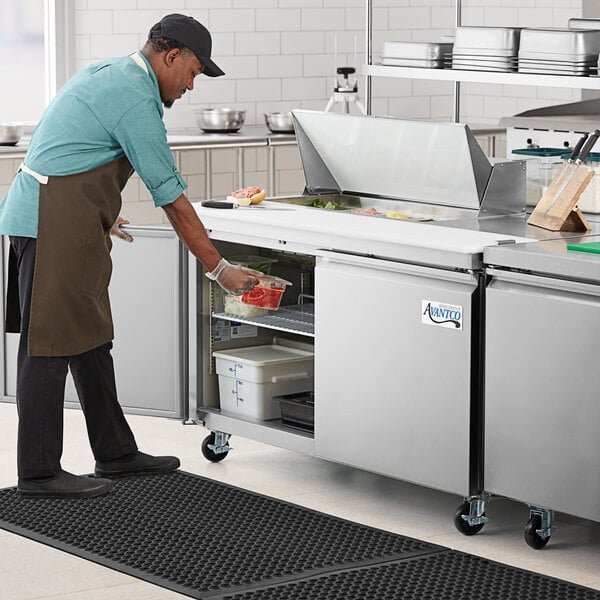 A man in an apron using an Avantco stainless steel refrigerator to prepare sandwiches.