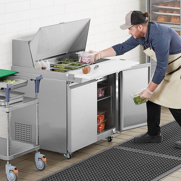 A man in an apron using an Avantco sandwich prep table to store food.