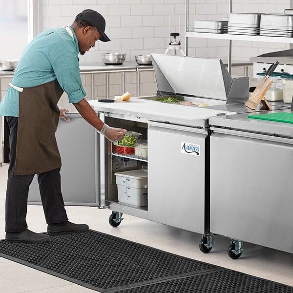 A man in an apron using an Avantco stainless steel sandwich prep table to prepare food.