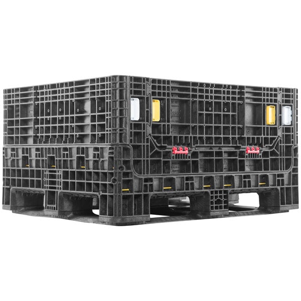 A black Orbis collapsible container with two yellow handles on a black plastic pallet.