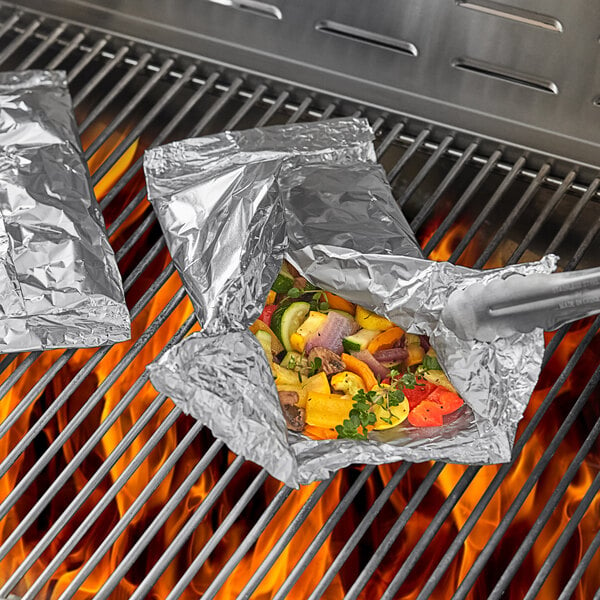 Two foil packets of food cooking on a grill.