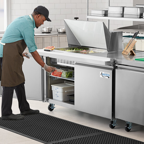 A man using an Avantco stainless steel sandwich prep table to prepare food.