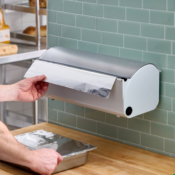 A wall-mounted plastic film and foil dispenser and cutter being used to cover a food tray with foil.
