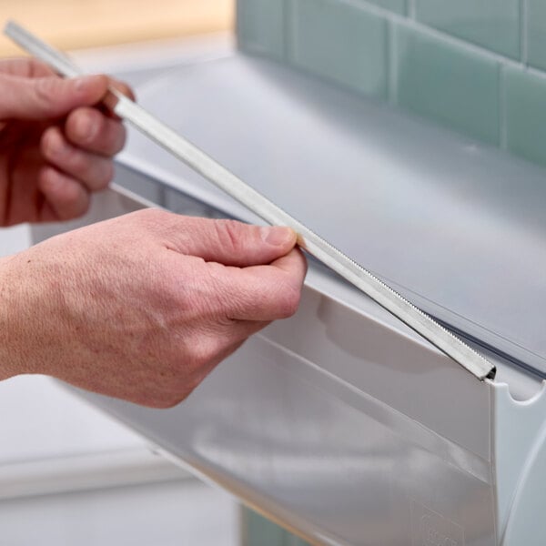 A person using a plastic film and foil dispenser with a built-in cutter.