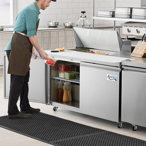 A man in a brown apron using an Avantco stainless steel sandwich prep refrigerator to store food.