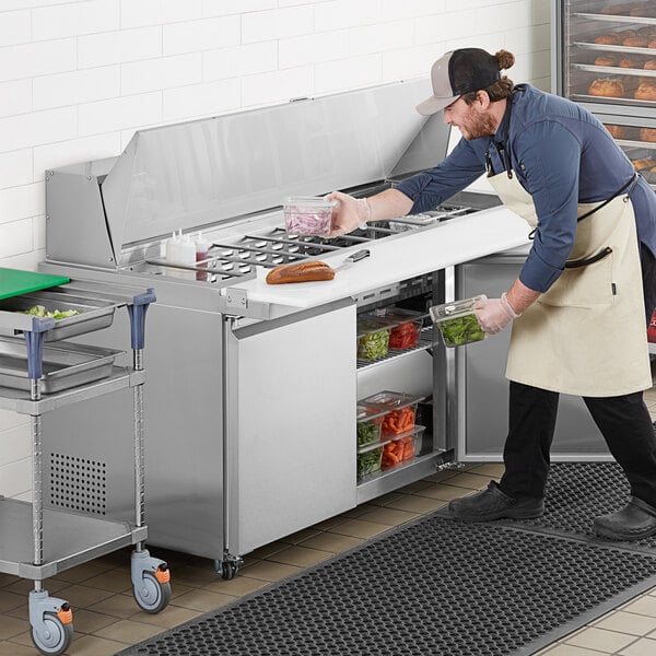 A man in an apron and gloves using an Avantco stainless steel sandwich prep table.