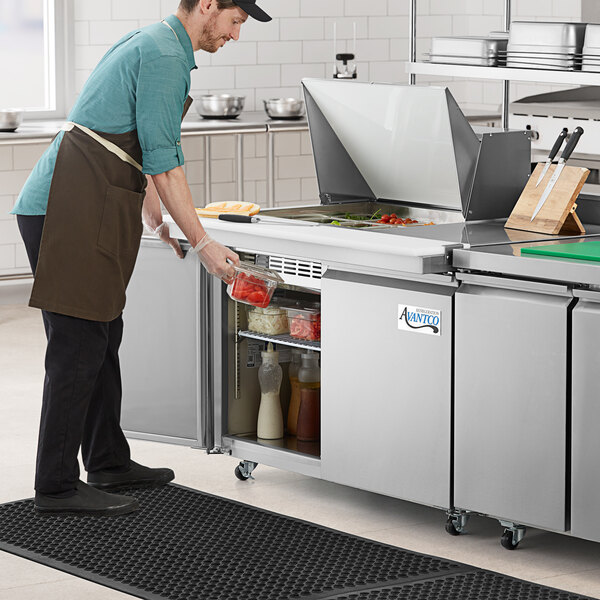 A man preparing food on an Avantco stainless steel sandwich prep table in a professional kitchen.