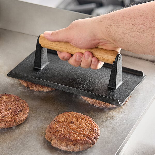 A person using an American Metalcraft steak weight to cook hamburgers on a grill.
