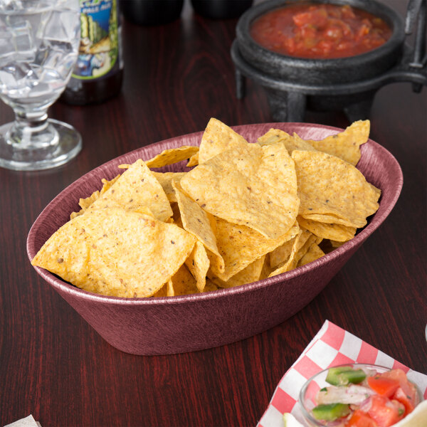A raspberry polyethylene oval basket filled with tortilla chips on a table in a Mexican restaurant.