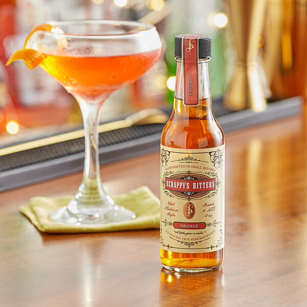 A bottle of Scrappy's Orange Bitters on a table next to a glass of liquid.