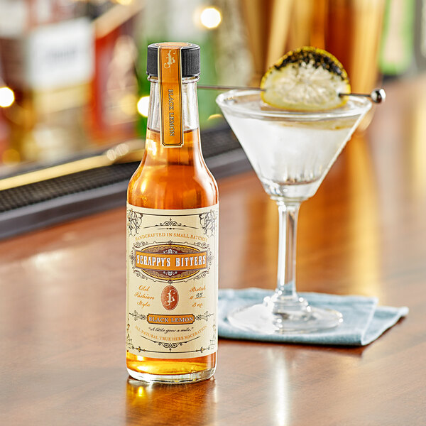 A bottle of Scrappy's Black Lemon Bitters next to a drink in a glass.