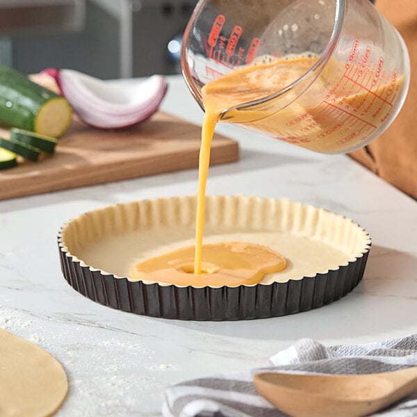 A round fluted non-stick tart or quiche pan with a removable bottom being filled with an egg mixture.