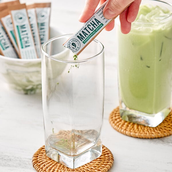 A hand holding a Jade Leaf Organic Ceremonial Matcha Single Serve Stick over a glass of matcha.