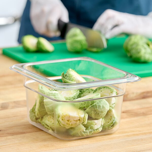 A person cutting up brussels sprouts in a Cambro plastic food pan on a counter.