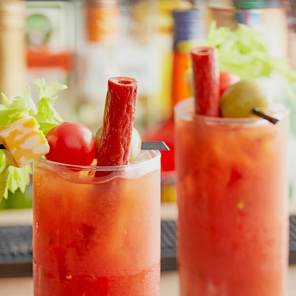 Two Bloody Mary drinks garnished with tomatoes, olives, and Benny's Original Meat Straws on a table in a brunch café.