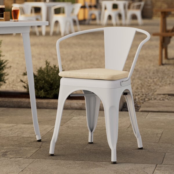 A Lancaster Table & Seating white outdoor arm chair with a tan cushion on a patio.