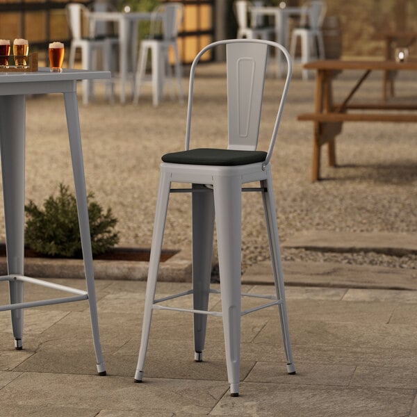 Two Lancaster Table & Seating metal bar stools with black cushions on an outdoor patio.