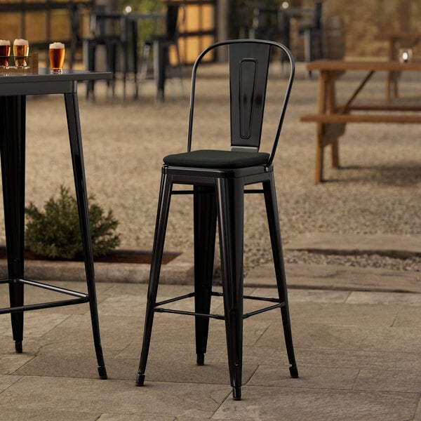 A black metal Lancaster Table & Seating outdoor cafe barstool with a black cushion.