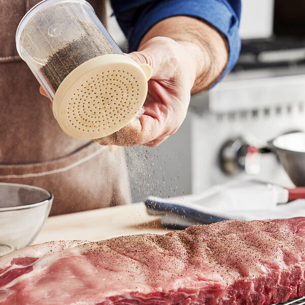 A person using a Choice beige polycarbonate shaker to sprinkle spices over a piece of meat.