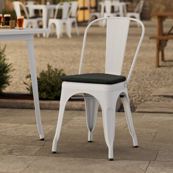 A Lancaster Table & Seating white outdoor cafe chair with a black cushion on a patio.