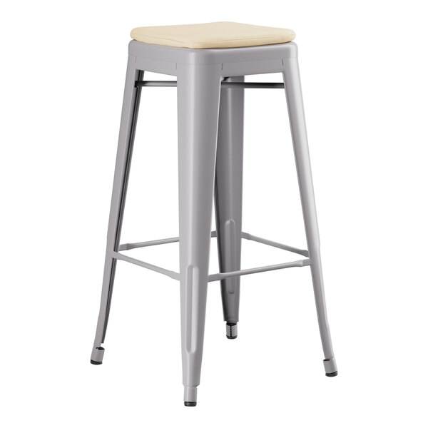 A grey Lancaster Table & Seating outdoor backless barstool with a tan cushion.